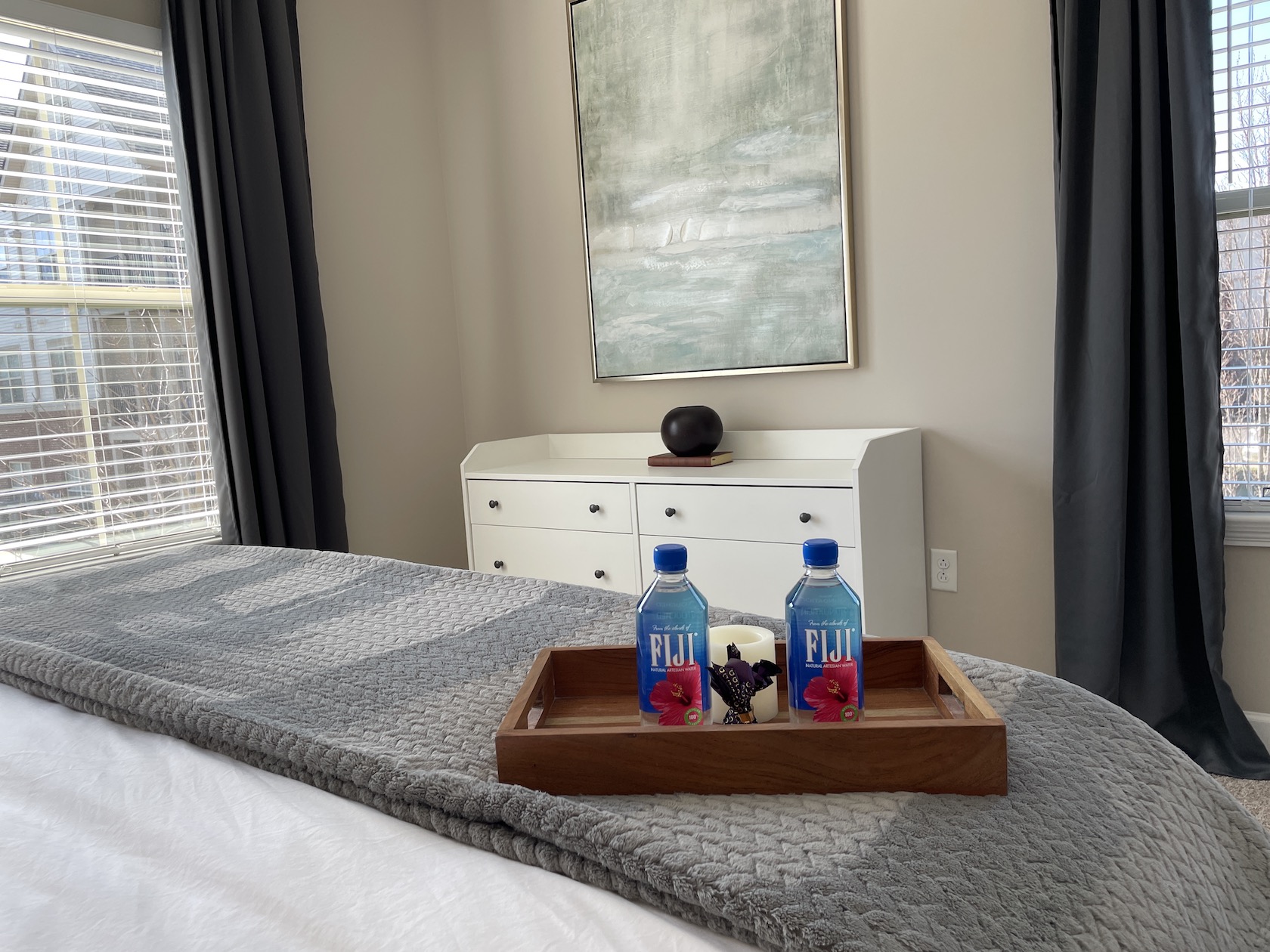 Two Fiji waters, chocolates, and a candle on a bed tray in the bedroom of a furnished apartment in Westerville ohio