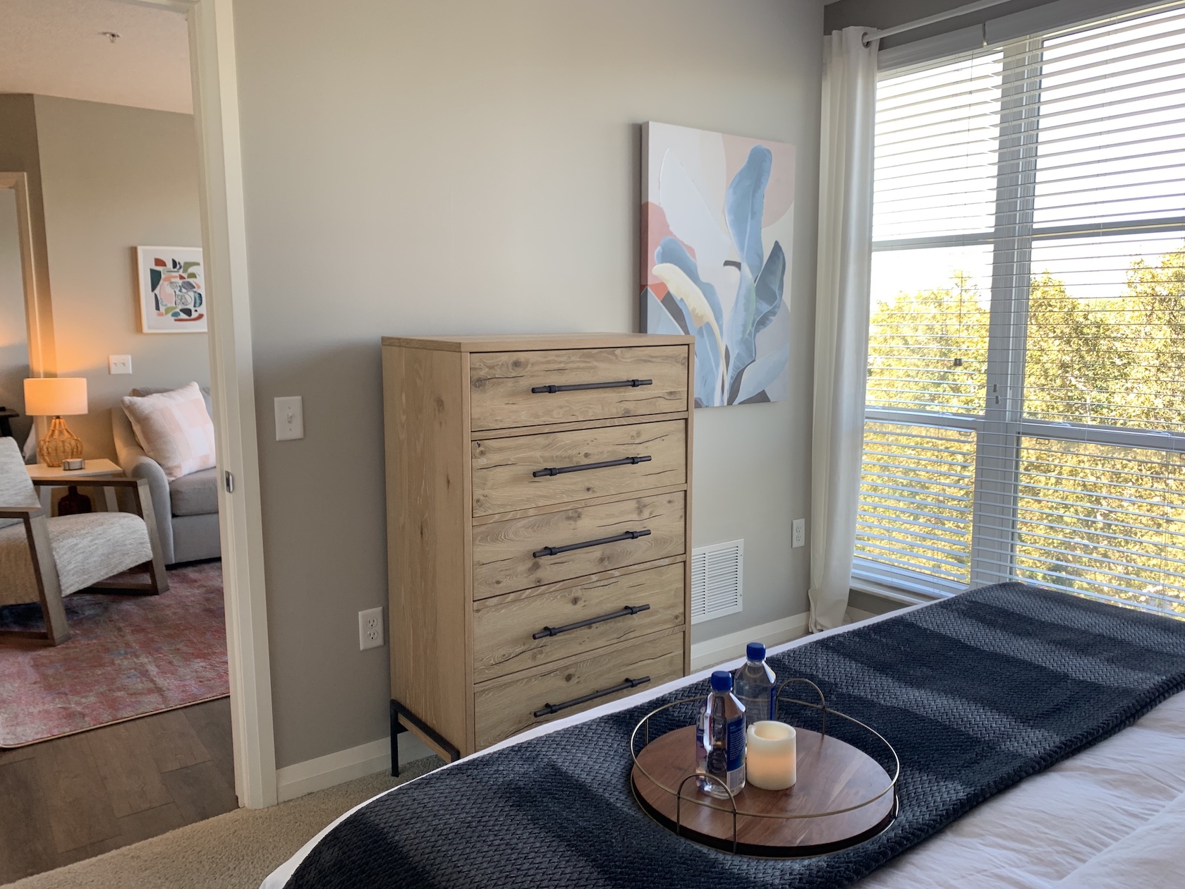 A bedroom with a king bed, a chest of drawers, and large windows in a furnished apartment in Downtown Columbus