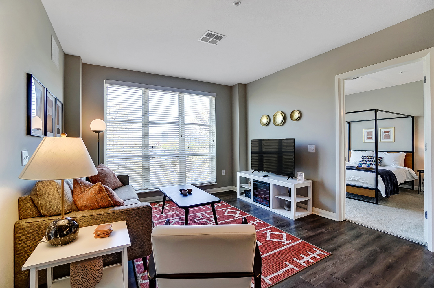 Living room with a smart tv, coffee table, couch, chair, large windows and red rug in a furnished apartment in Downtown Columbus