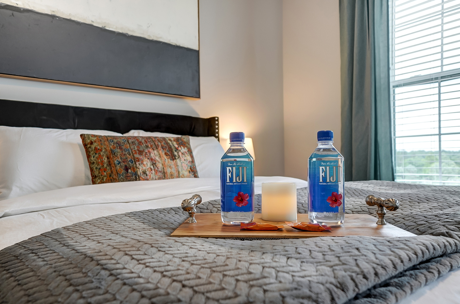 Two bottles of Fiji water, chocolates, and a candle on a bed tray in a furnished apartment near OSU