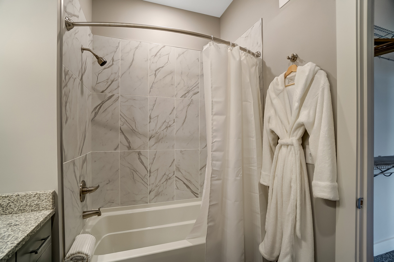 Shower tub combo with an Epicurean branded Frette robe hanging from the wall of a furnished apartment near OSU