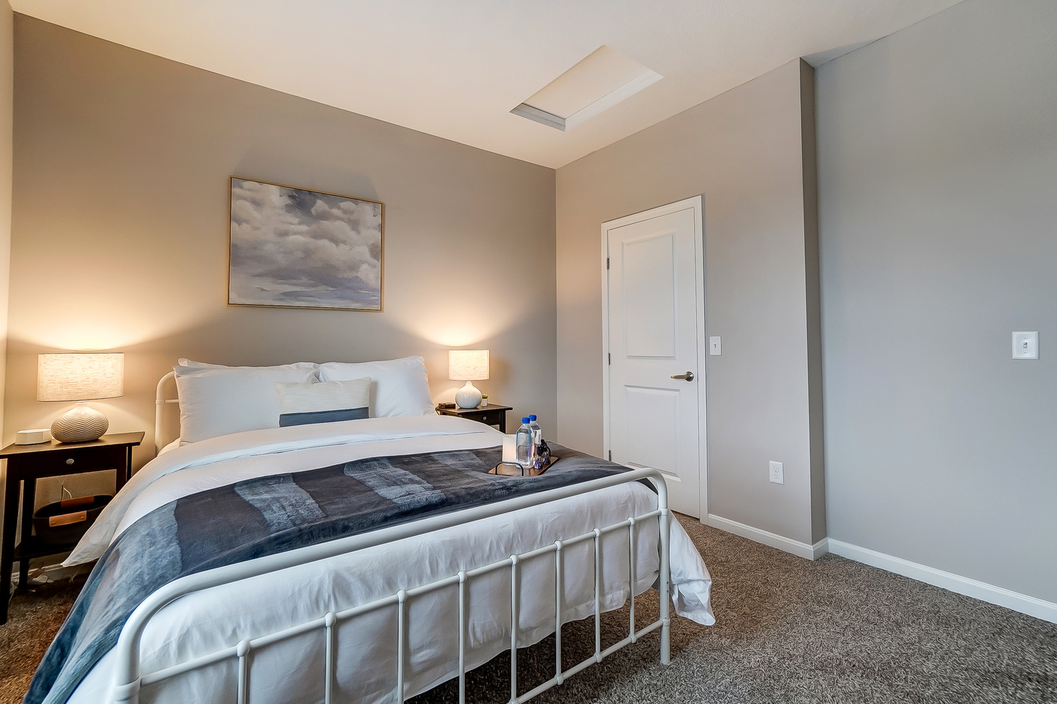 A queen bed with a nightstand, a lamp, and wall art in a furnished apartment near New Albany Ohio