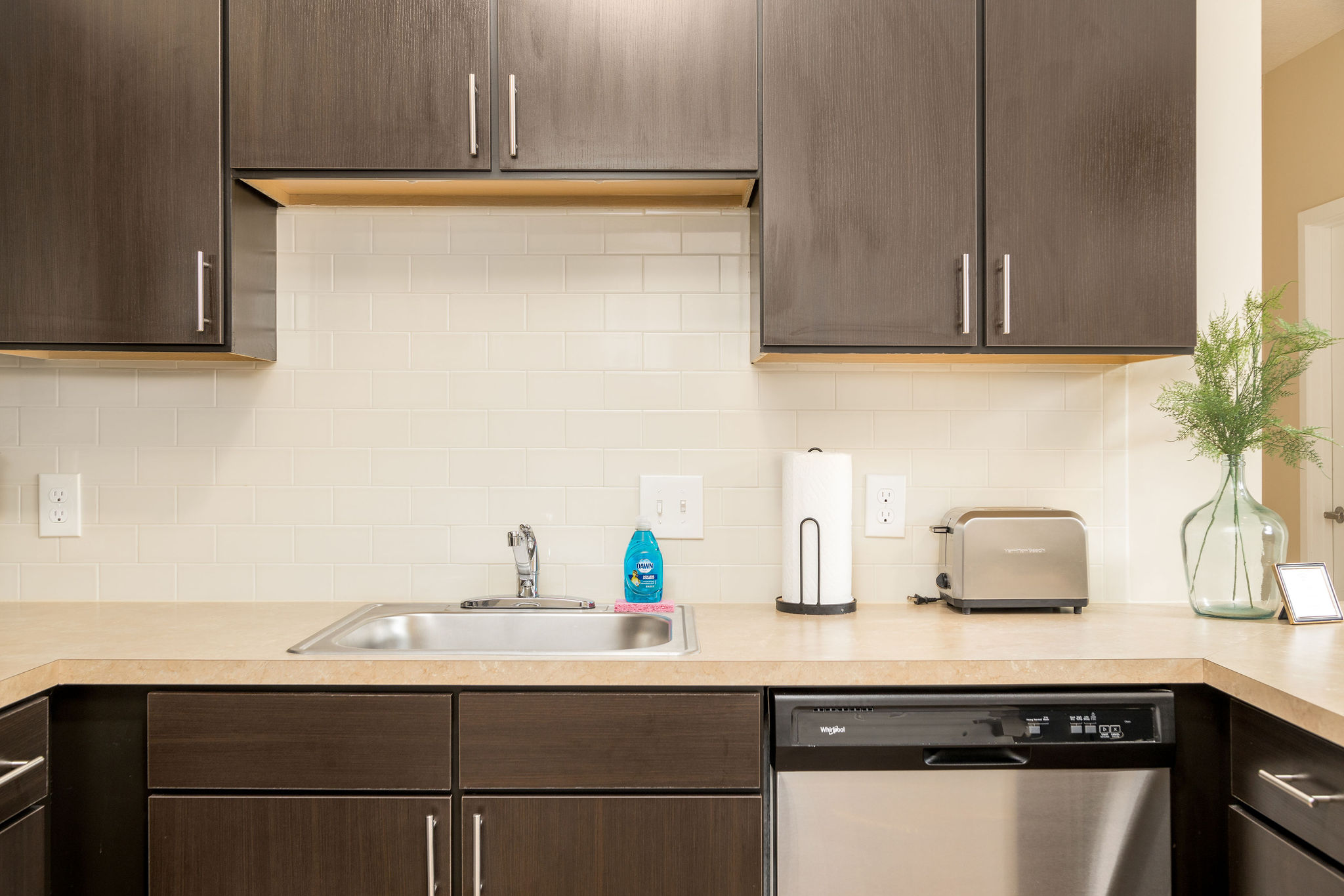 A kitchen counter with a sink and stainless steel dishwasher in a furnished apartment near New Albany Ohio