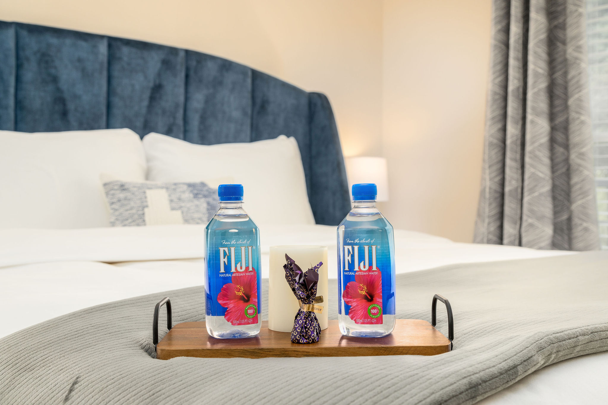 Two bottles of Fiji water, chocolates, and a candle on a bed tray in a furnished apartment near New Albany Ohio