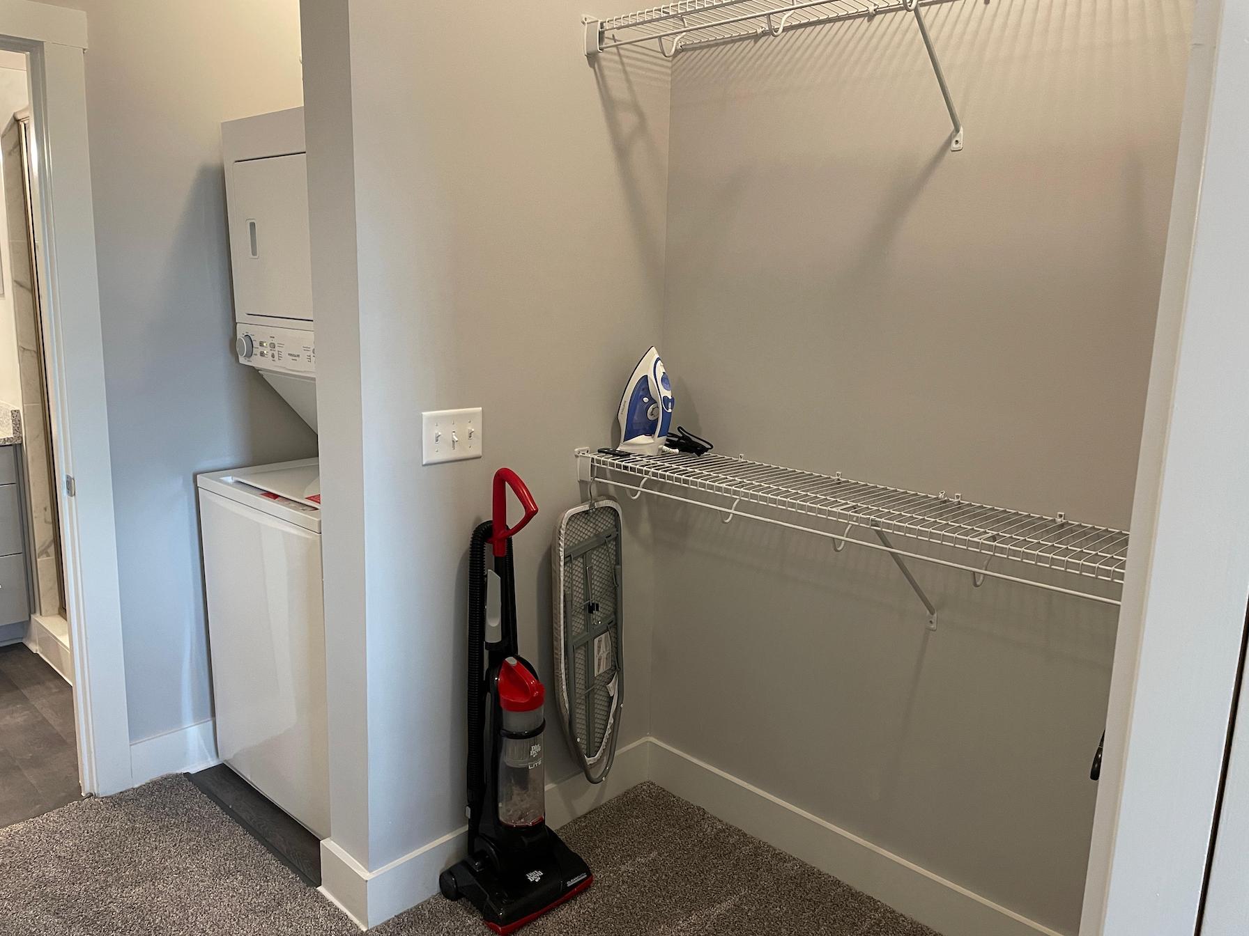 Apartment closet with a vacuum, iron and ironing board, and washer and dryer in a furnished apartment near Ohio State