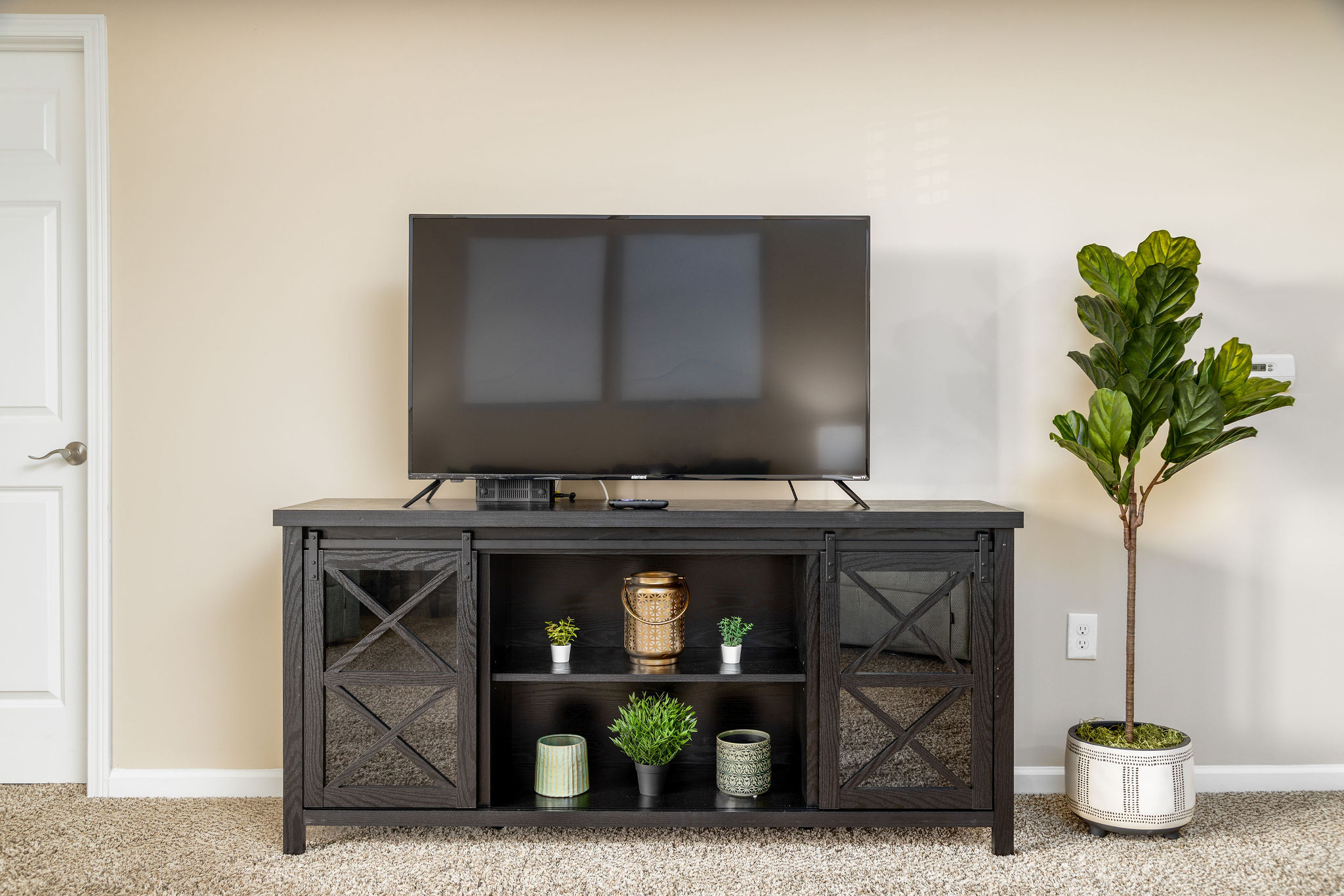 A smart tv on a tv stand next to a faux plant in a furnished apartment near New Albany Ohio