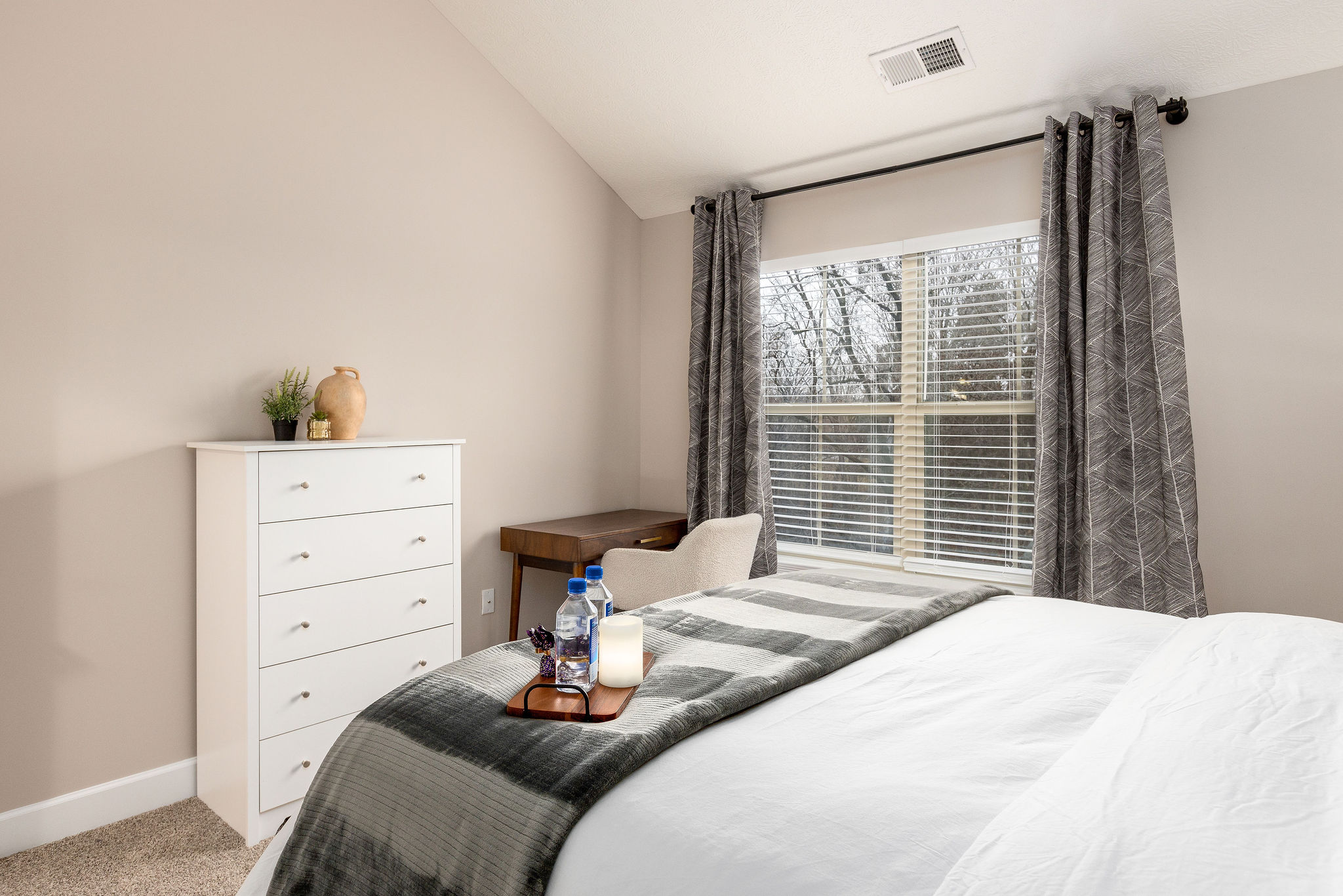 A bedroom with a chest of drawers, a desk, and desk chair