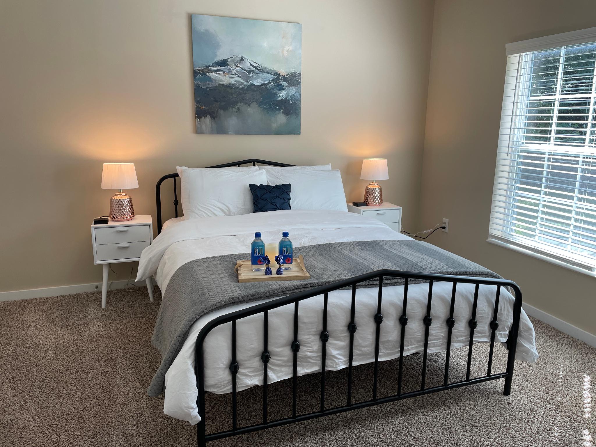 Queen bed in a guest bedroom with wall art, nightstands and lamps in a furnished apartment near New Albany Ohio