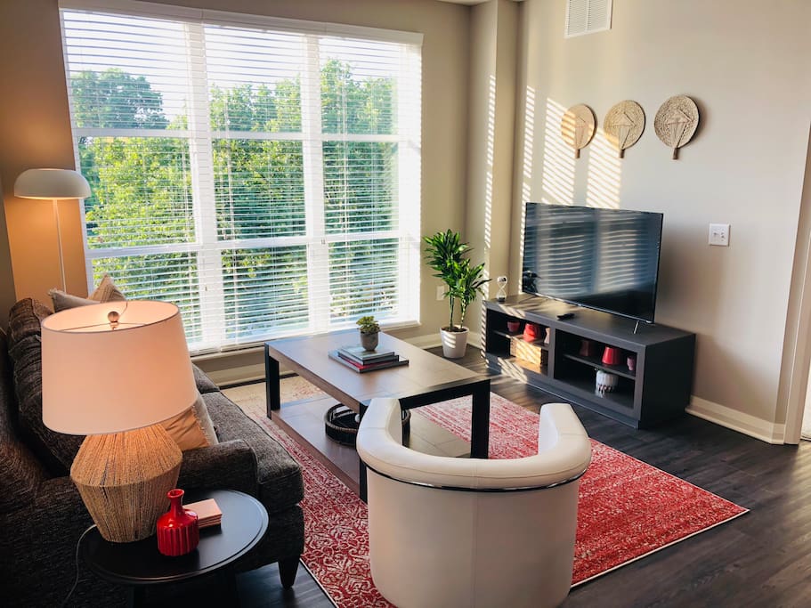 Living room with a smart tv, coffee table, couch, chair, large windows and red rug in a furnished apartment in Downtown Columbus