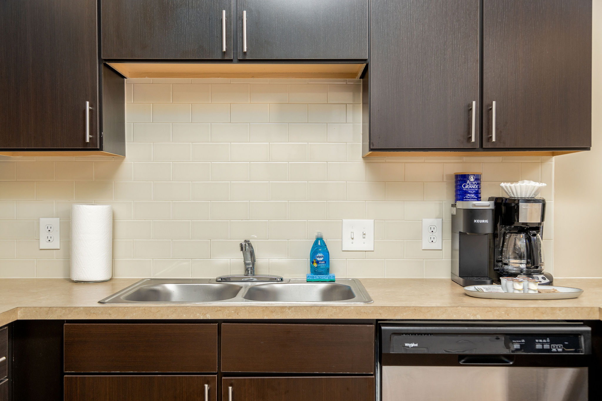 A kitchen counter with a sink and stainless steel dishwasher in a furnished apartment near New Albany Ohio