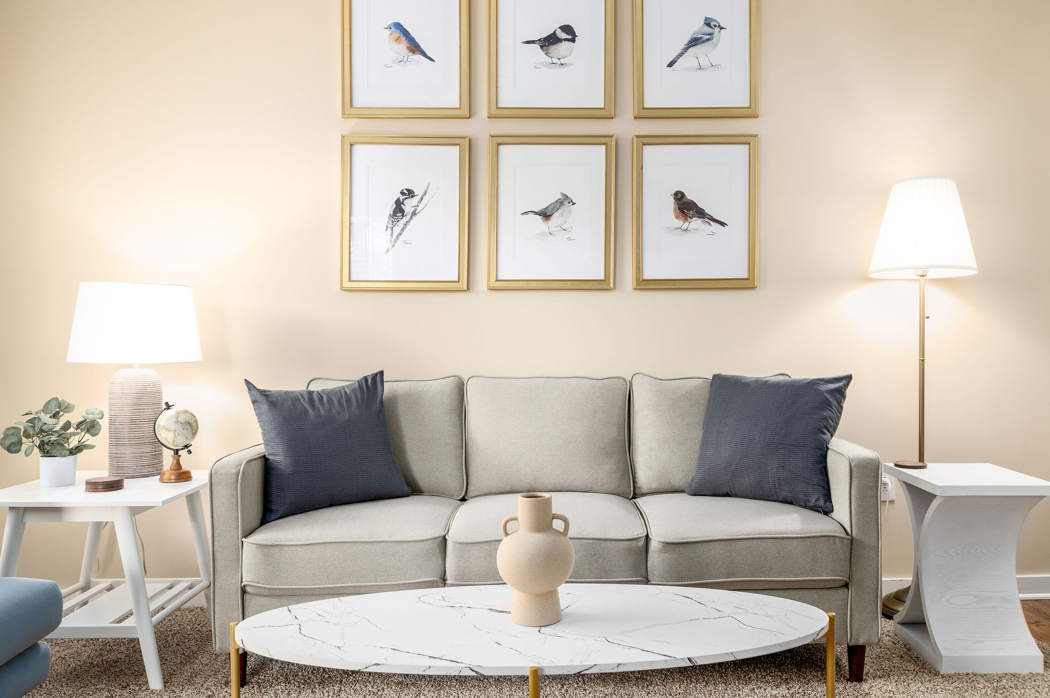 A cream couch with a coffee table and photos of birds in a gallery above in a furnished apartment near New Albany Ohio