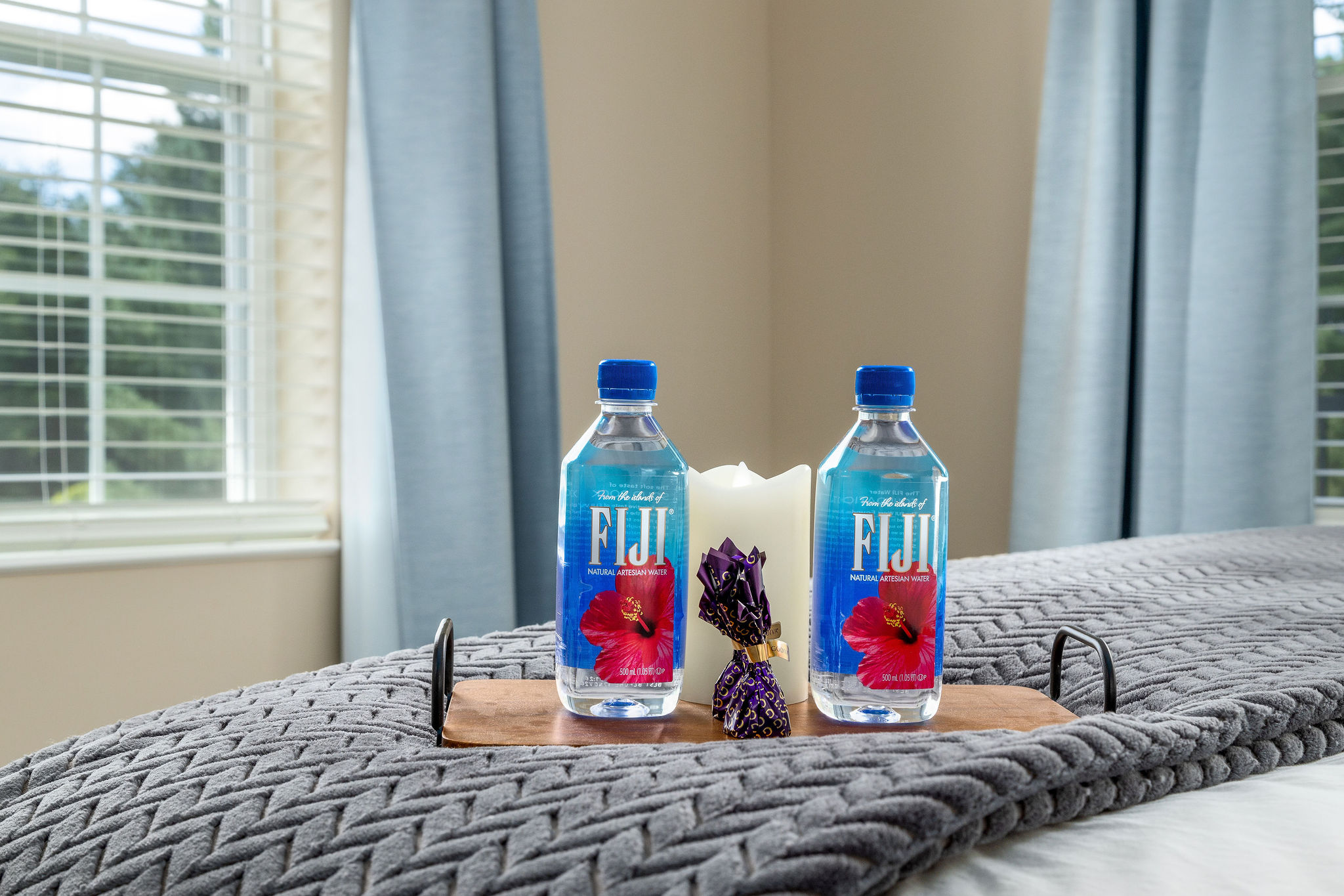 Two bottles of Fiji water, chocolates, and a candle on a bed tray in a furnished apartment near New Albany Ohio