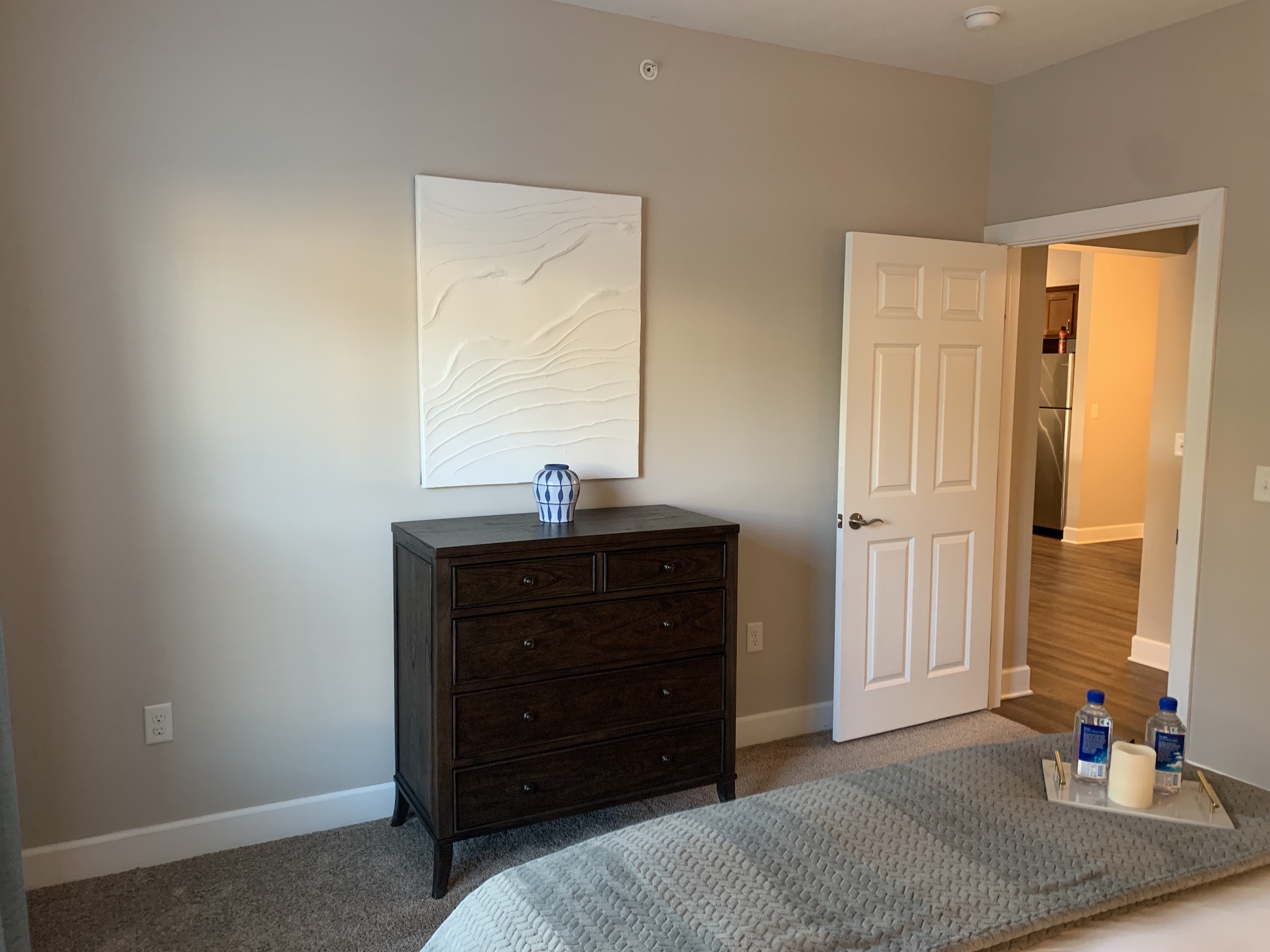 A bedroom with a queen bed, chest of drawers, and wall art in a furnished apartment in Westerville Ohio