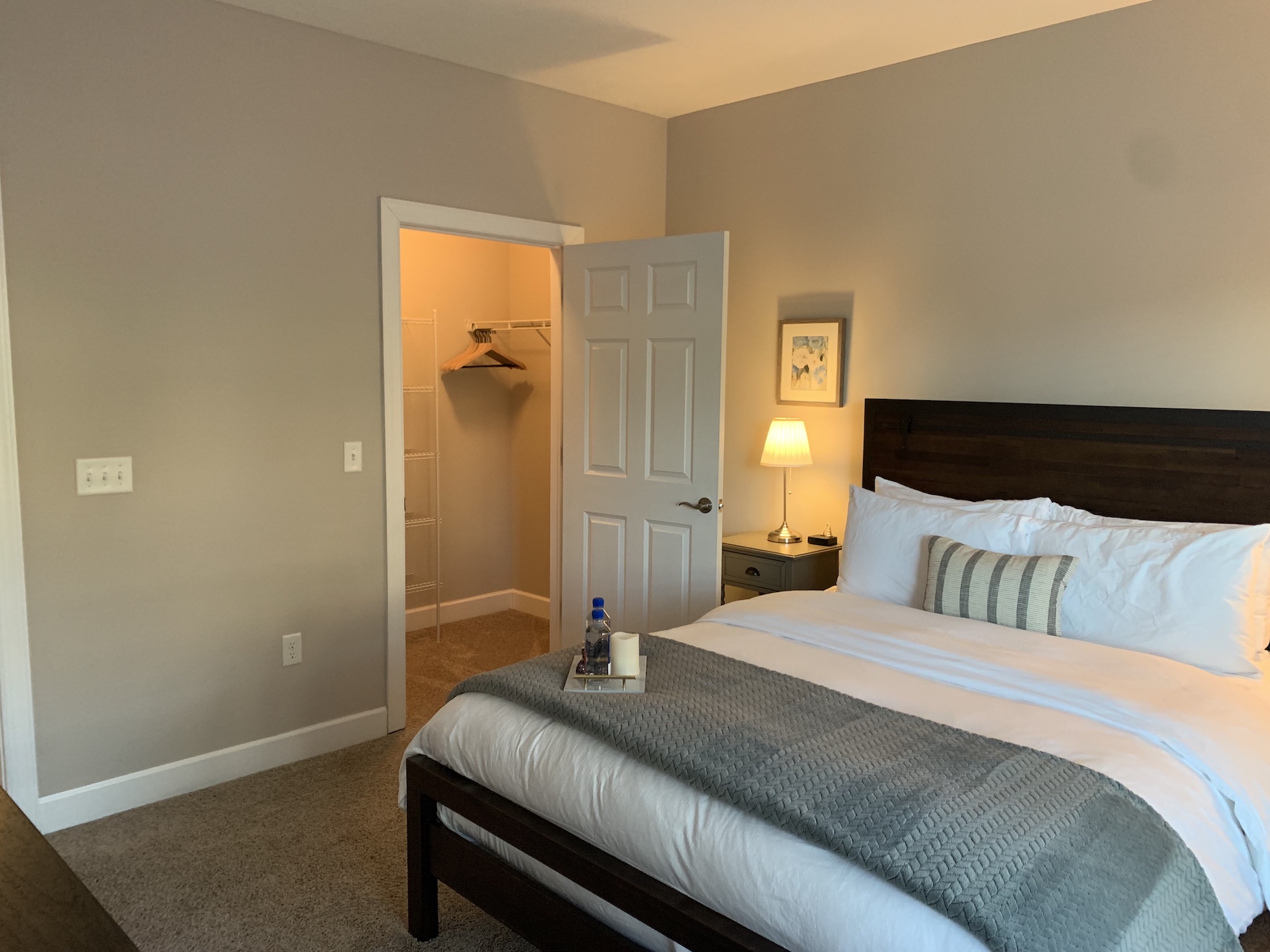 A queen bed in a bedroom with wall art, lamps, and nightstands in a furnished apartment in Westerville Ohio