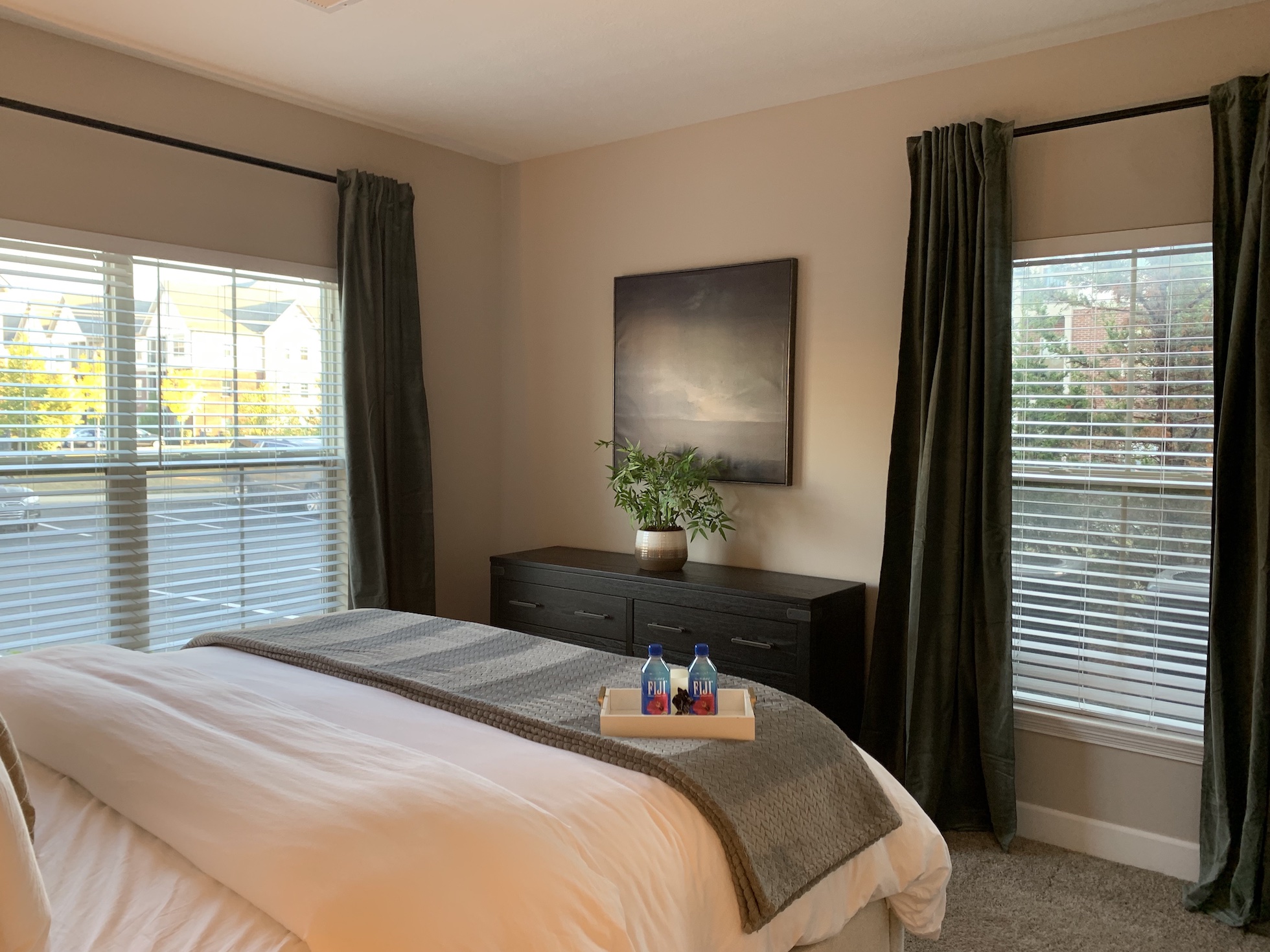 A bedroom in a furnished apartment in Westerville Ohio with a king bed, curtains, a dresser, and wall art