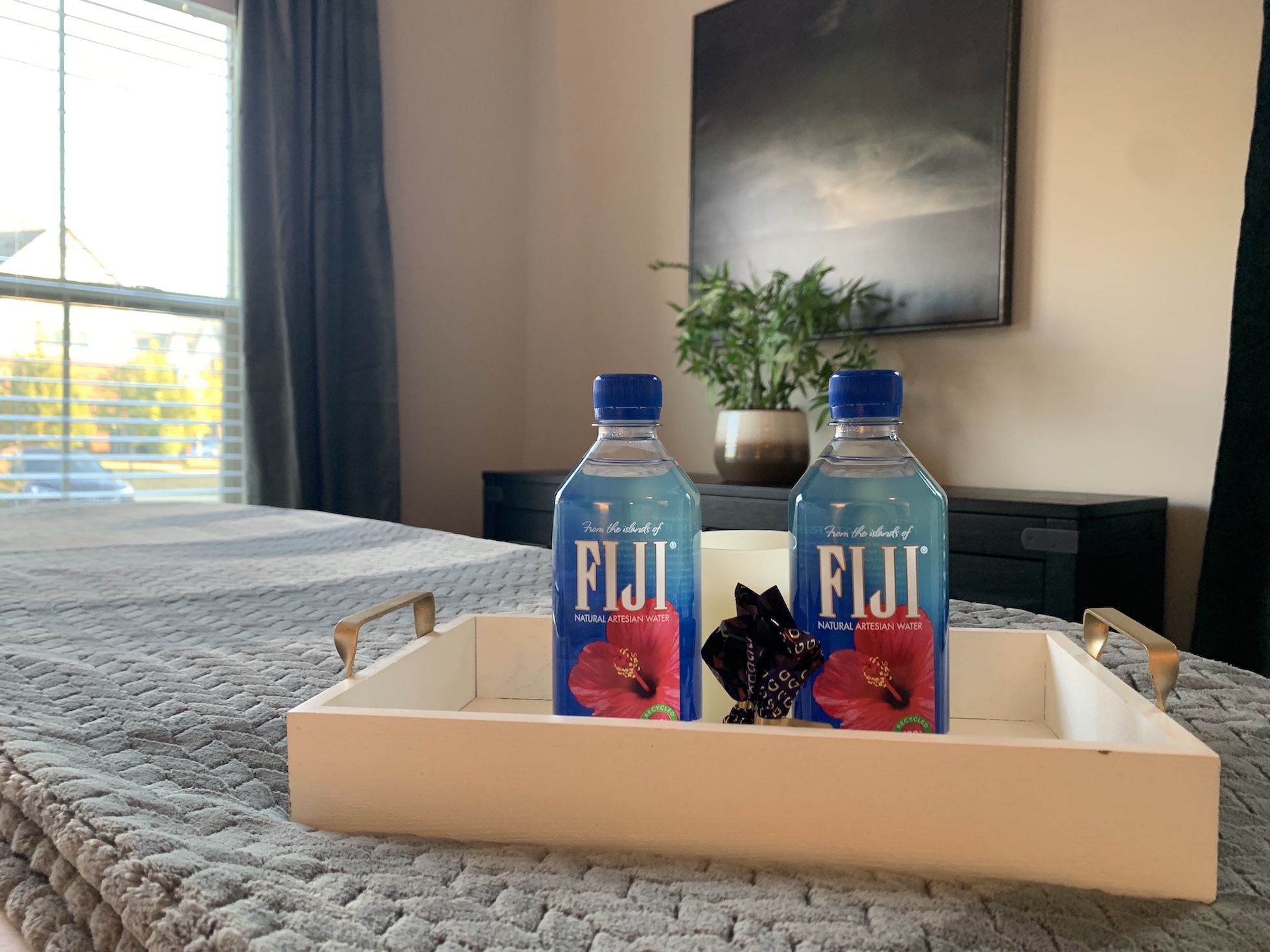 Two Fiji waters, chocolates, and a candle on a bed tray in the bedroom of a furnished apartment in Westerville ohio