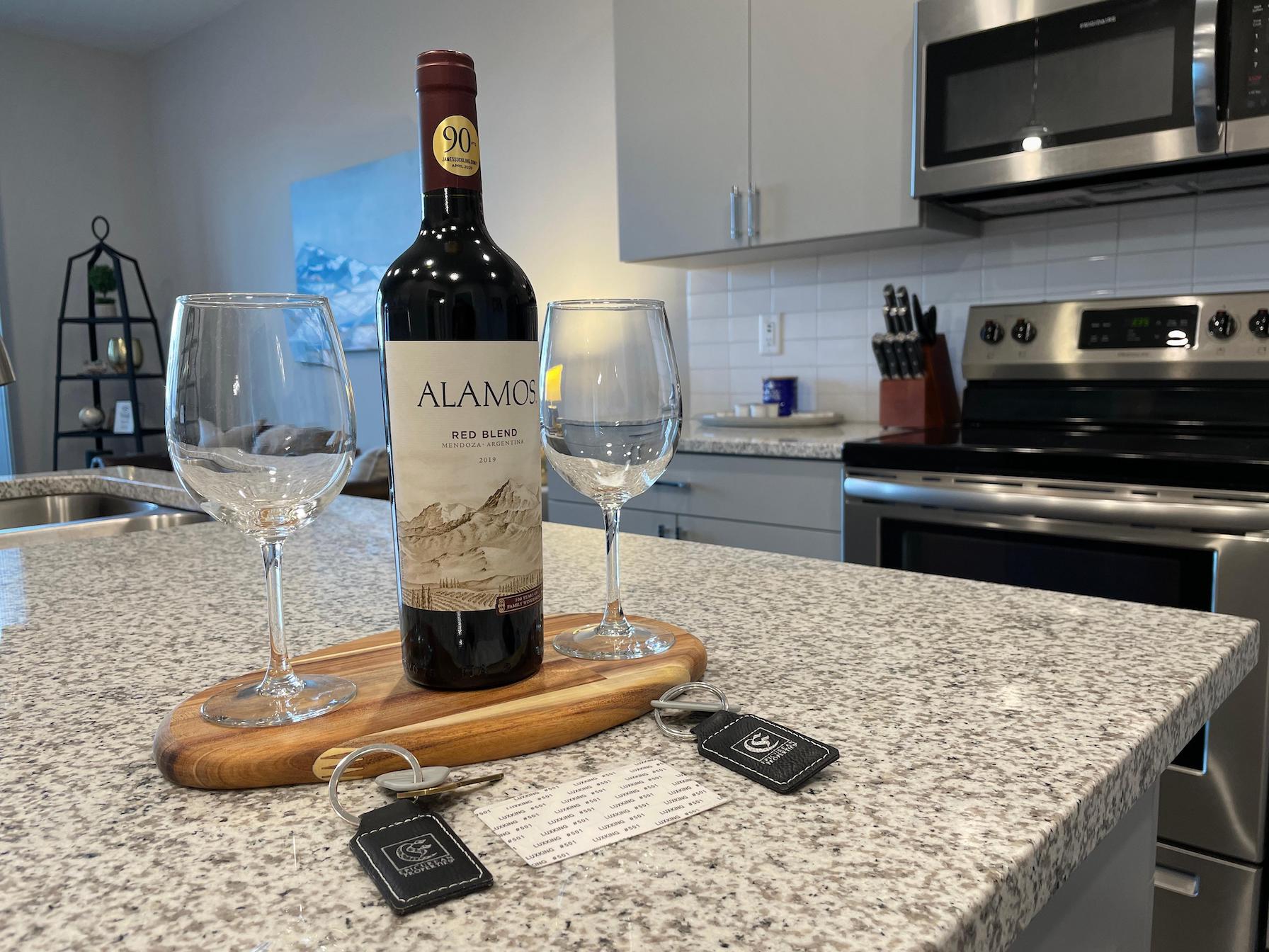 A bottle of wine and two clean wine glasses on the kitchen counter of a furnished apartment near Ohio State