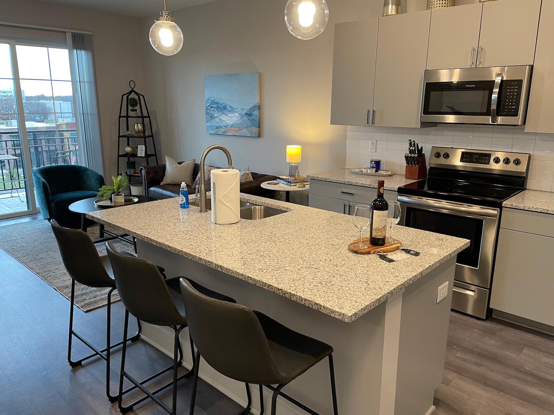 Kitchen island with counter stools and a sink in the kitchen of a furnished apartment near Ohio State