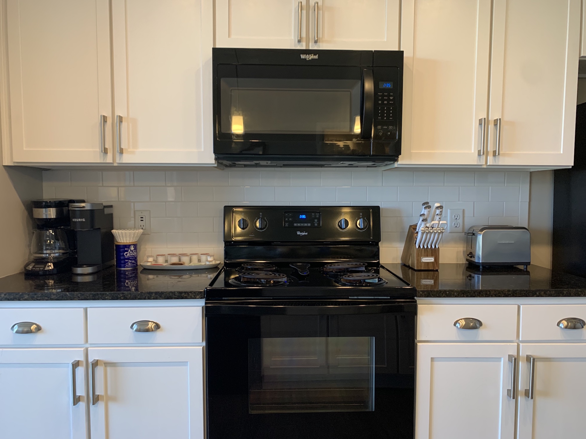 A kitchen with white cabinets and black appliances in a furnished apartment in Downtown Columbus